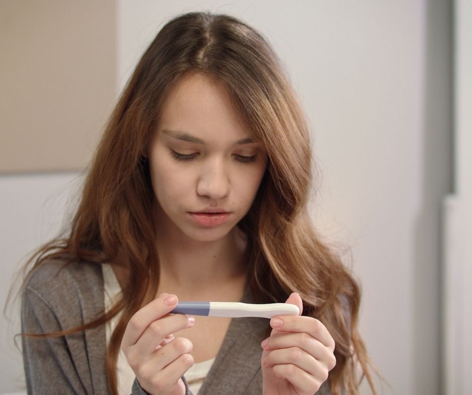 Young woman looking at a pregnancy test, she looks concerned, scared, worried.