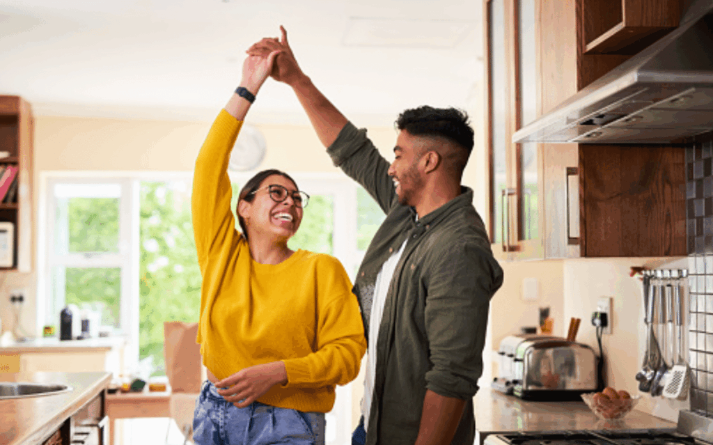 Smiling couple dancing together in a bright kitchen.