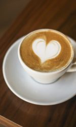 Espresso coffee with heart shaped froth art on a wooden table in a cafe.