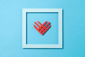 Giving Tuesday, global day of charitable giving after Black Friday shopping day. Charity, give help, donations support concept. Red paper heart and empty blue frame on blue background. Top view, copy space, flat lay.
