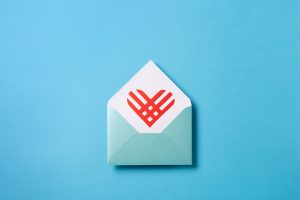 Giving Tuesday text. Global day of charitable giving after Black Friday shopping day. Charity, give help, donations support concept. Red paper heart in blue empty envelope on blue background, top view